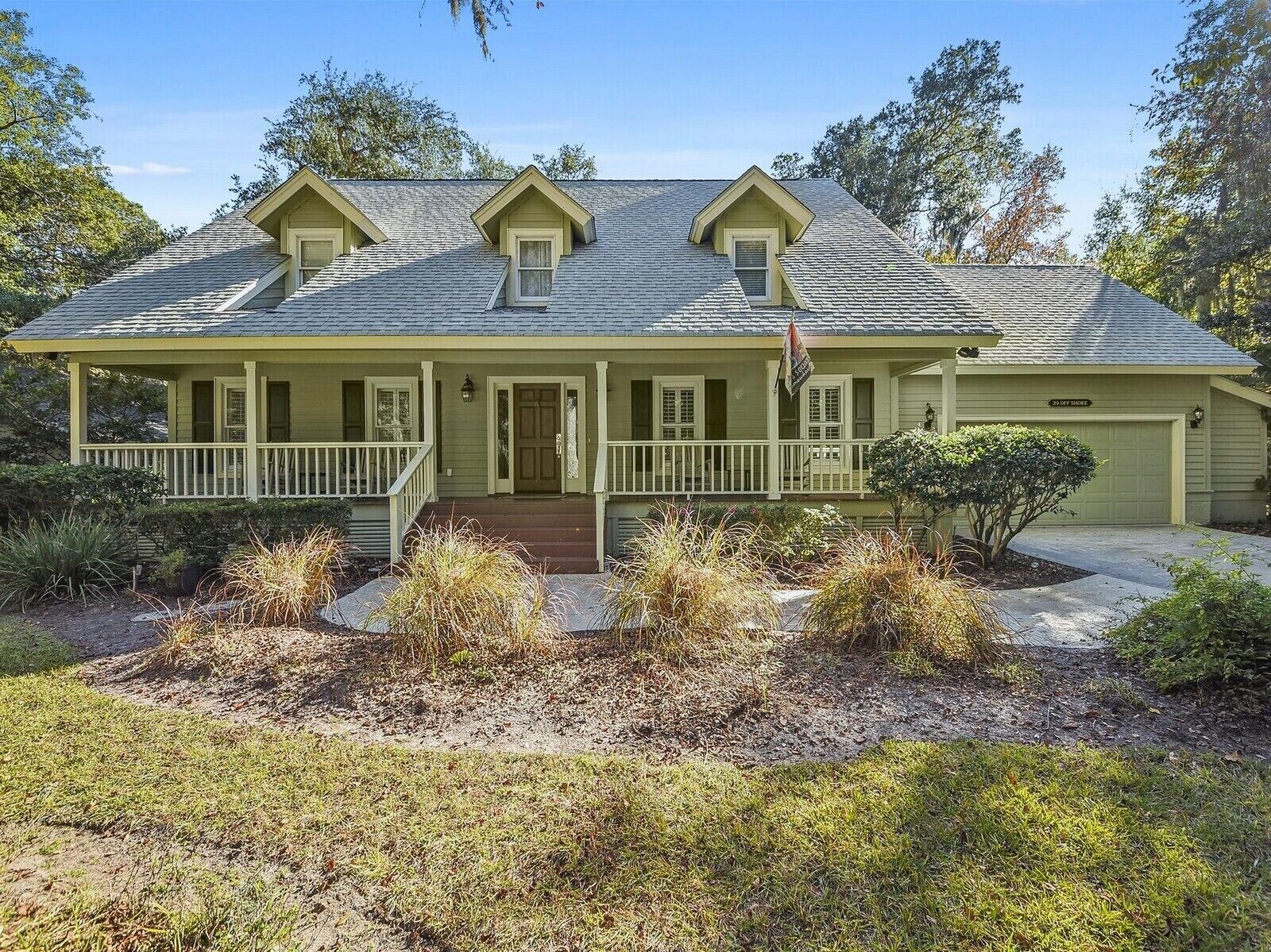 A two-story house with a front porch, a garage, and a small garden area with various plants.