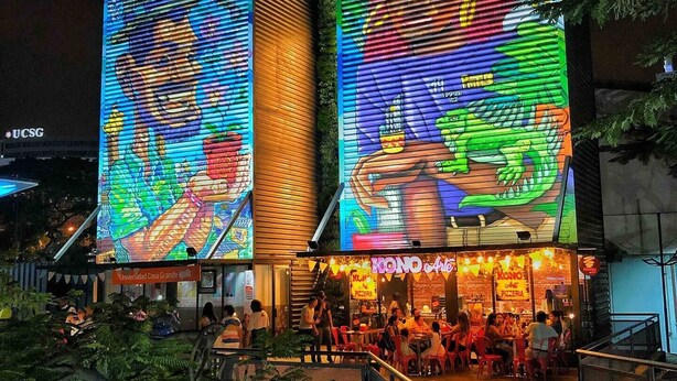 A building with large digital displays on the facade, a restaurant named 'KONO Arte' at the ground level, and people dining outside. - Encantador Dpto en Garzota norte  (Guayaquil)