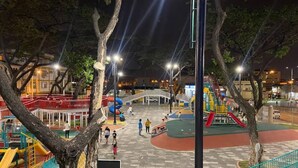 An outdoor playground at night with various play structures, including slides and climbing areas, surrounded by trees and street lamps. - Encantador Dpto en Garzota norte  (Guayaquil)