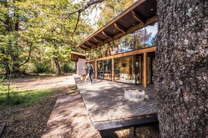 A modern wooden deck with glass walls, surrounded by trees. - Stylish cabin in Corralco with Hot Tub in the middle of the native forest. (Malalcahuello)