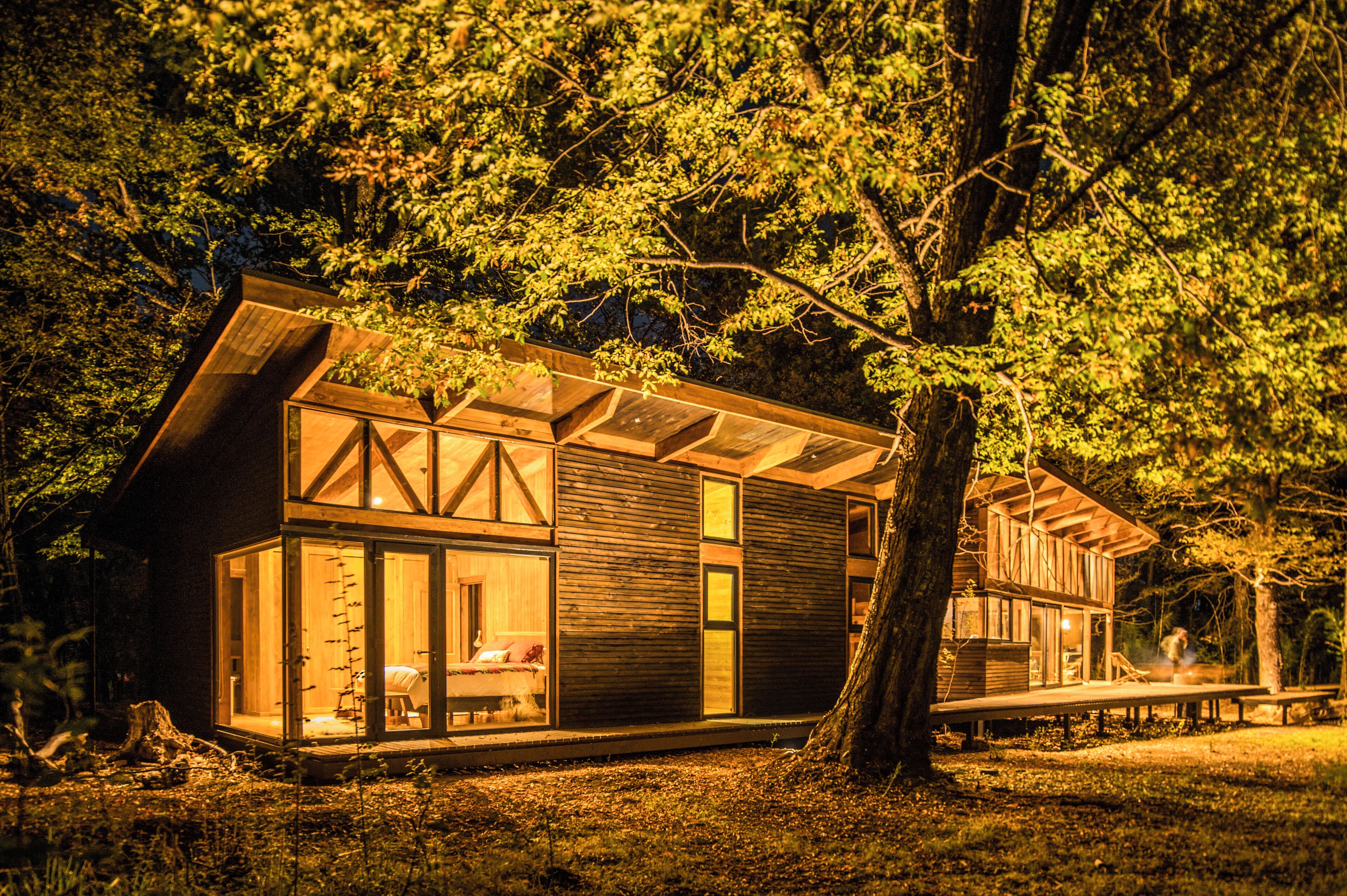 A modern cabin with a glass facade, wooden exterior, and a deck area.