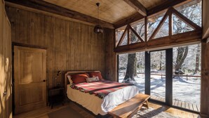 A wooden cabin bedroom with a bed, bench, and large windows overlooking a snowy landscape. - Stylish cabin in Corralco with Hot Tub in the middle of the native forest. (Malalcahuello)