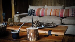 A cozy living room with a wooden coffee table, a cushioned sofa, and decorative items including a traditional South American drink container and pinecones. - Stylish cabin in Corralco with Hot Tub in the middle of the native forest. (Malalcahuello)