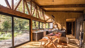 A spacious kitchen with large windows, a wooden dining table, and a bench. - Stylish cabin in Corralco with Hot Tub in the middle of the native forest. (Malalcahuello)