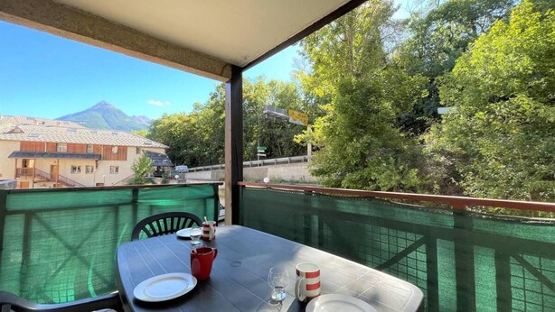 A balcony with a table set for two, overlooking a mountain and greenery.