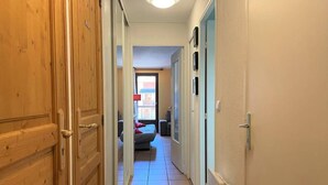A narrow hallway with wooden doors on one side and a bed with a red pillow in the room at the end.