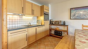 A compact kitchen with wooden cabinets, a tiled backsplash, a microwave, and a coffee maker. - Floor -2, view mountain, swimming pool, balcony, tv, ski locker, 70m², Les Arcs (Bourg-Saint-Maurice)