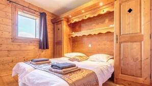 A wooden cabin room with a bed, two towels, a window with curtains, and wooden walls. - Floor -2, view mountain, swimming pool, balcony, tv, ski locker, 70m², Les Arcs (Bourg-Saint-Maurice)