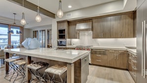 A modern kitchen with a large island, bar stools, stainless steel appliances, and wooden cabinets.