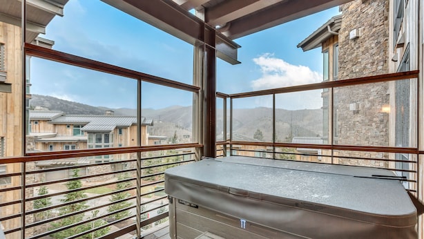 A balcony with a view of a mountainous landscape, a stone building, and a modern outdoor heater.