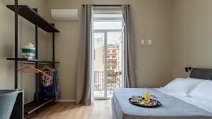 A hotel room with a bed, a desk, a chair, a hanging clothes rack, and a balcony with a view of buildings. - moris  (Palermo)