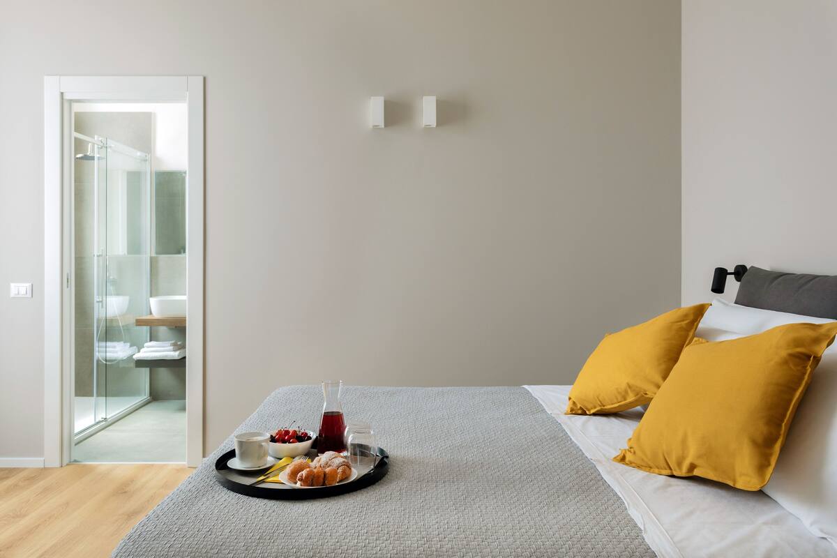 Une chambre d’hôtel moderne avec un lit, un plateau de petit-déjeuner comprenant des viennoiseries, un bol de fruits et une bouteille de jus de fruits.
