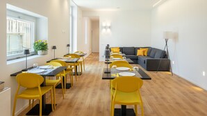 A modern dining area with yellow chairs and tables, a gray sofa with yellow cushions, and a potted plant by the window. - moris  (Palermo)