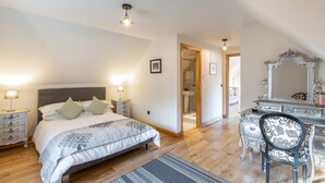 A bedroom with a bed, bedside tables, a dresser, a mirror, and a door leading to another room. - The Stables - near St Andrews Sleeps 10 (Fife)