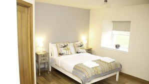 A neatly arranged bedroom with a bed, bedside tables, and a window. - The Stables - near St Andrews Sleeps 10 (Fife)