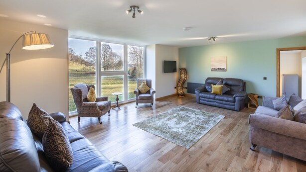A spacious living room with a large window, leather sofas, a floor lamp, and a decorative rug. - The Stables - near St Andrews Sleeps 10 (Fife)