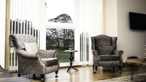 A room with two armchairs, a small round table, and a TV mounted on the wall. - The Stables - near St Andrews Sleeps 10 (Fife)