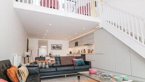 Sala de estar moderna com sofá de couro preto, mesa de centro de vidro e escada que leva a um andar superior.