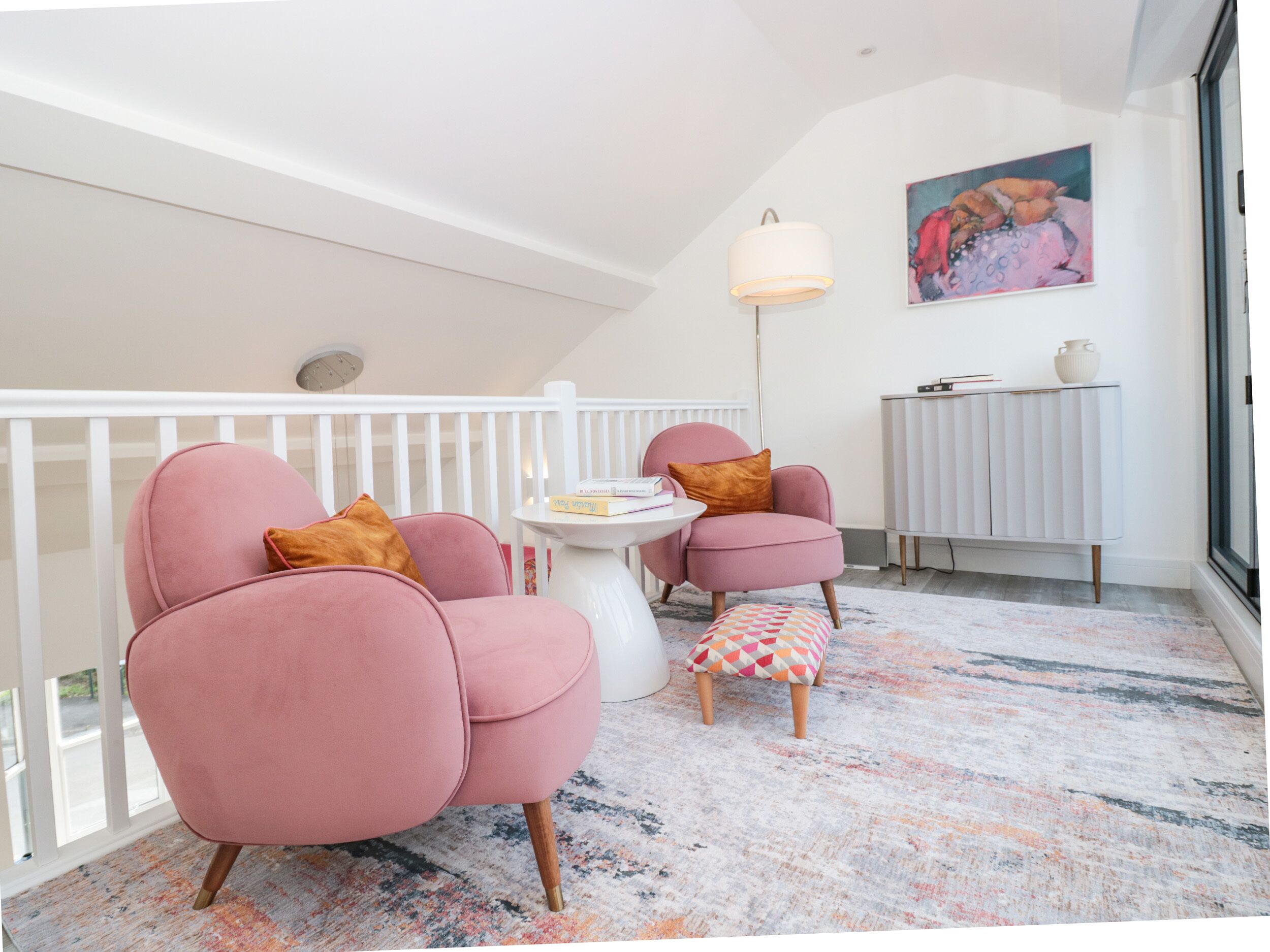 Een moderne woonkamer met roze fauteuils, een kleine ronde tafel en een kleurrijk vloerkleed.