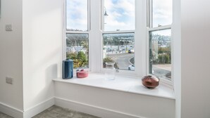 Quarto de canto com três janelas, vista para uma marina e uma estrada.