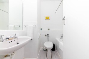 A bathroom with a white sink, toilet, and bathtub. There is a towel rack above the sink and a small shelf with toiletries. - Boho Chic Studio Apartment in Cape Town (Cape Town)