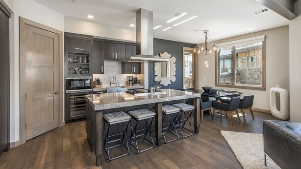 Una cocina moderna con armarios de madera oscura, una isla central con taburetes y un comedor con candelabro.