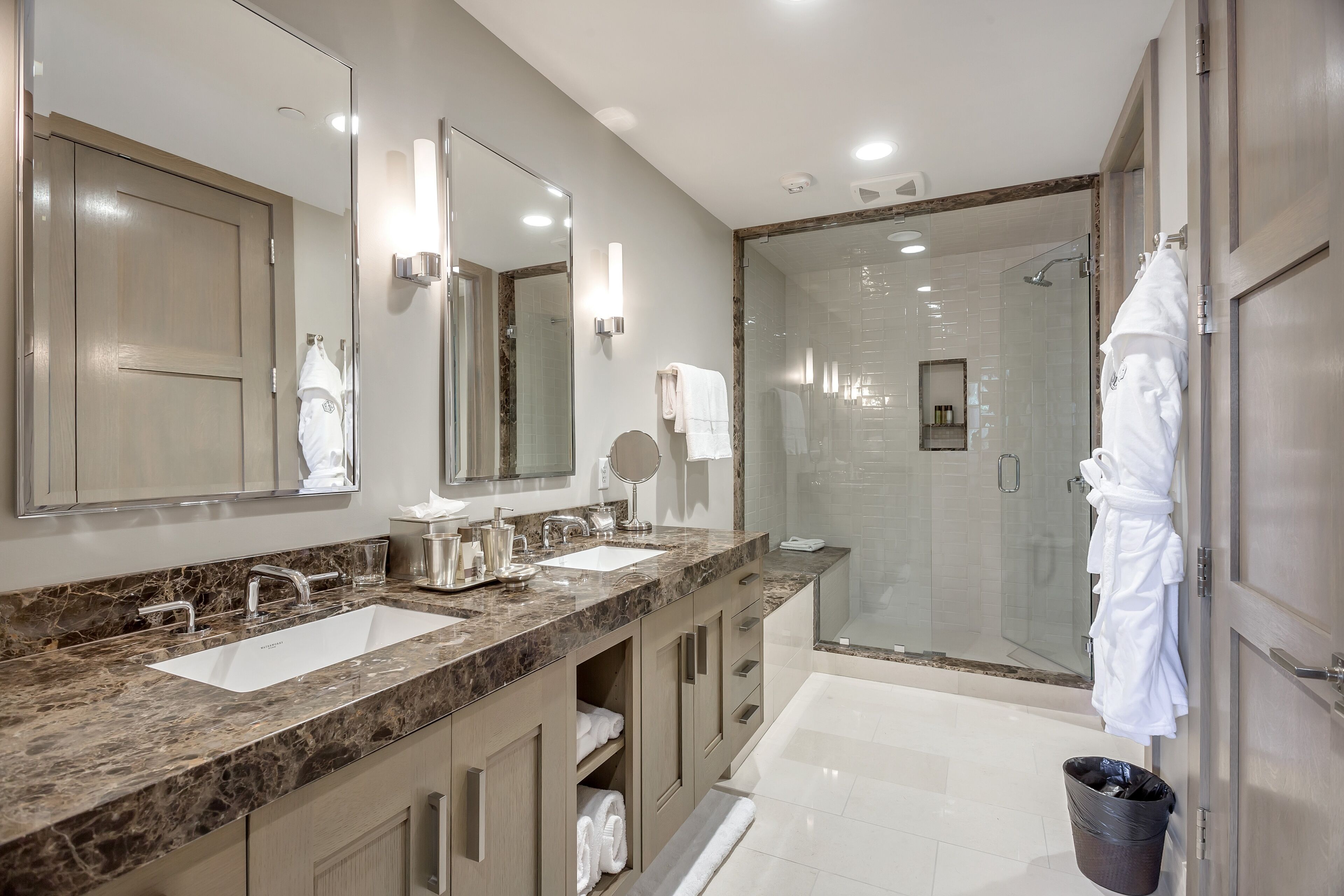 A modern bathroom with two sinks, a large mirror, and a walk-in shower.
