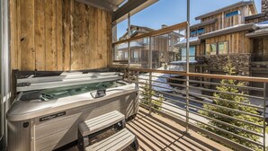 Zona de spa con jacuzzi y asientos en una terraza de madera, con vistas a una zona residencial.