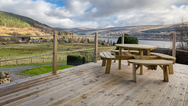 A wooden deck with picnic tables overlooking a scenic landscape with hills and a body of water. - Ciaran Cottage (Aberfeldy)