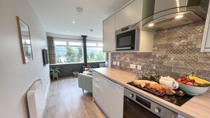 A modern kitchen with a built-in oven, microwave, and a large window overlooking a garden. - Ciaran Cottage (Aberfeldy)