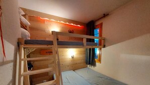 A bunk bed room with a ladder, a small window with curtains, and a wall-mounted light fixture.