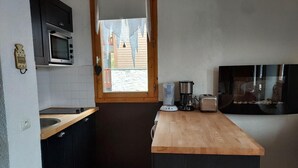A compact kitchen with a microwave, coffee maker, toaster, and a window with a view of a building outside.