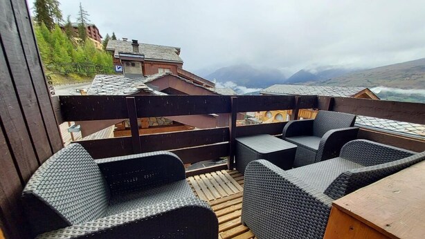 An outdoor seating area with wicker furniture and a wooden deck overlooking a mountainous landscape.
