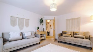 Een woonkamer met twee banken, een witte vloerkleden, macramé wanddecoraties en een hanglamp.