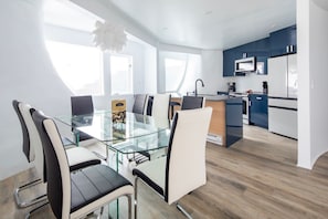 A modern kitchen with a glass dining table, white chairs, and blue cabinets.