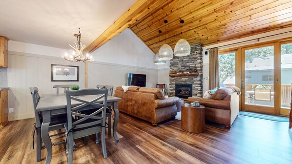 Amplia sala de estar con chimenea de piedra, techo de madera y comedor con mesa y sillas.