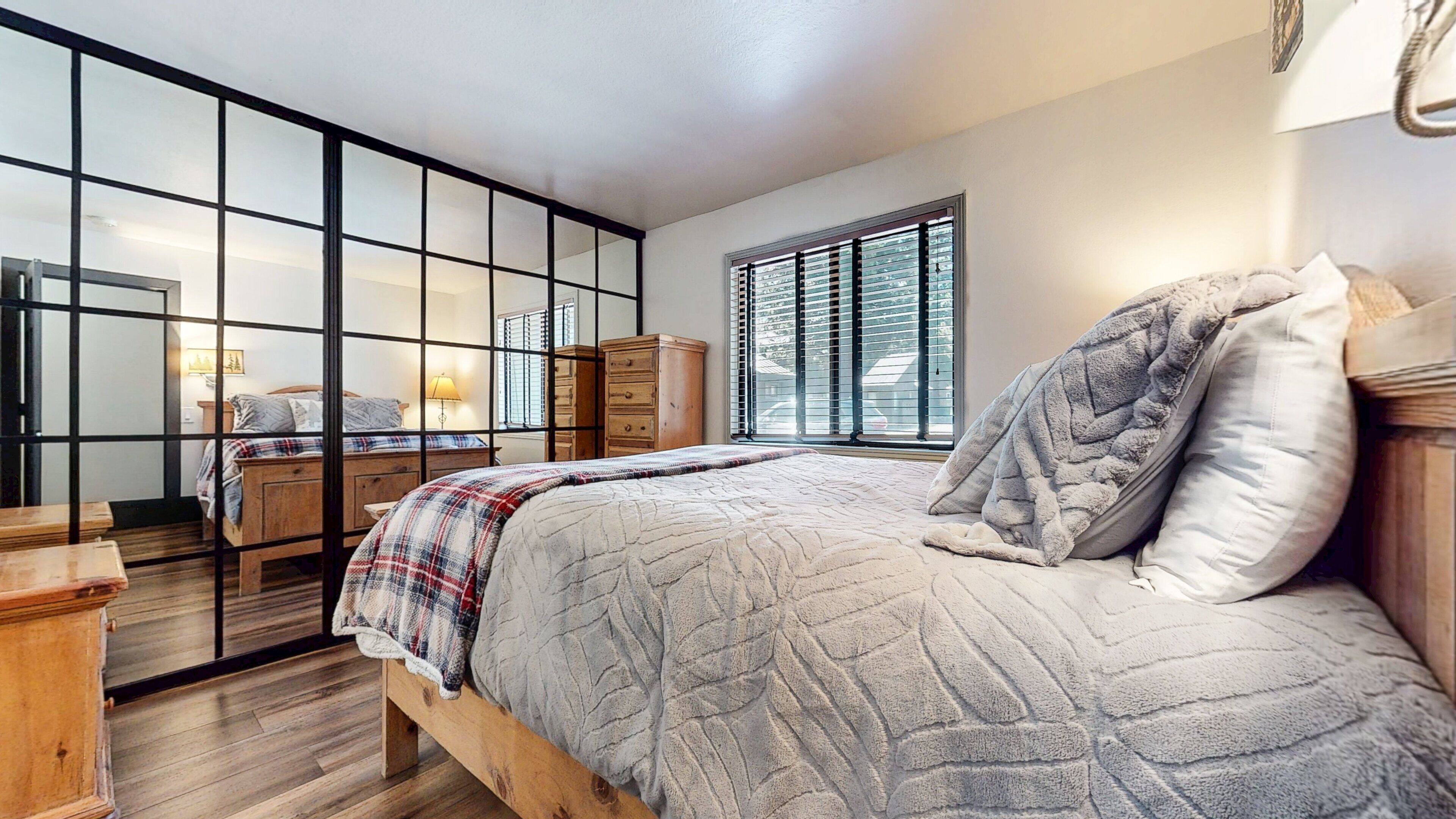 A bedroom with a bed, a dresser, a window with blinds, and a mirror.