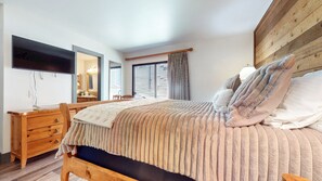 Un dormitorio con cama, cómoda de madera y televisor montado en la pared.