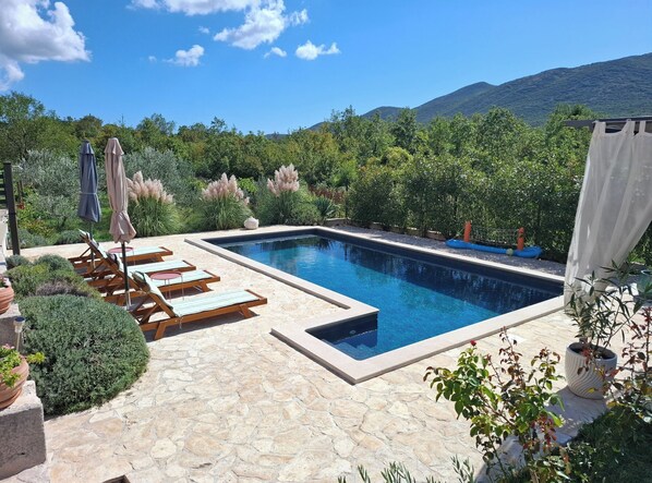 Une piscine entourée de verdure et de montagnes, avec des chaises longues et des parasols.