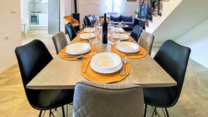 A dining area with a long table set for six, surrounded by black chairs, in a modern apartment with a kitchen and a staircase. - Villa Vinka (Vrgorac)