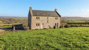 A stone house with a sloped roof, a small porch, and a view of rolling hills in the background. - Lower Cowden Farm (Bakewell)