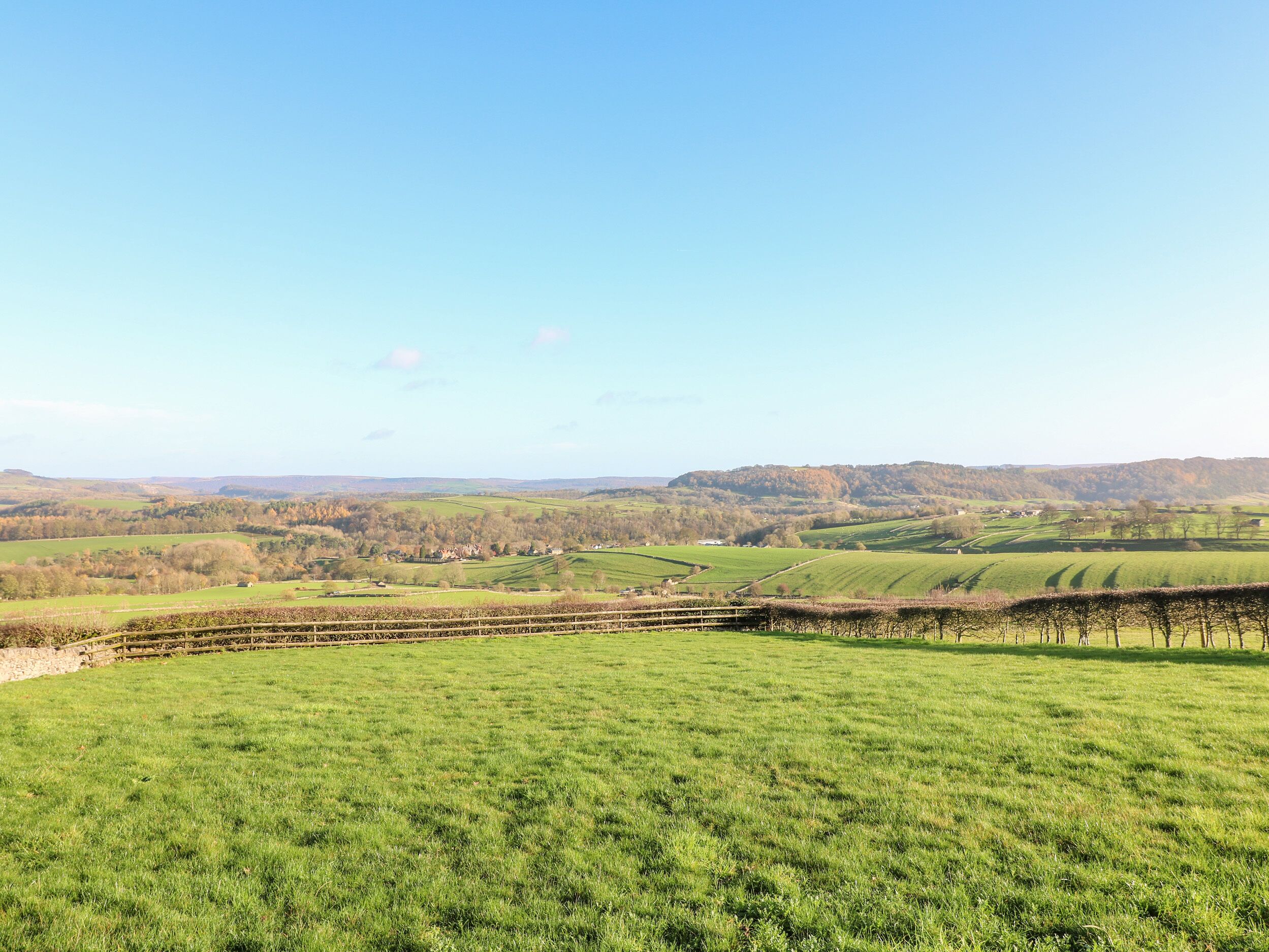 A rural landscape with rolling green fields, a stone wall, and a distant hill.