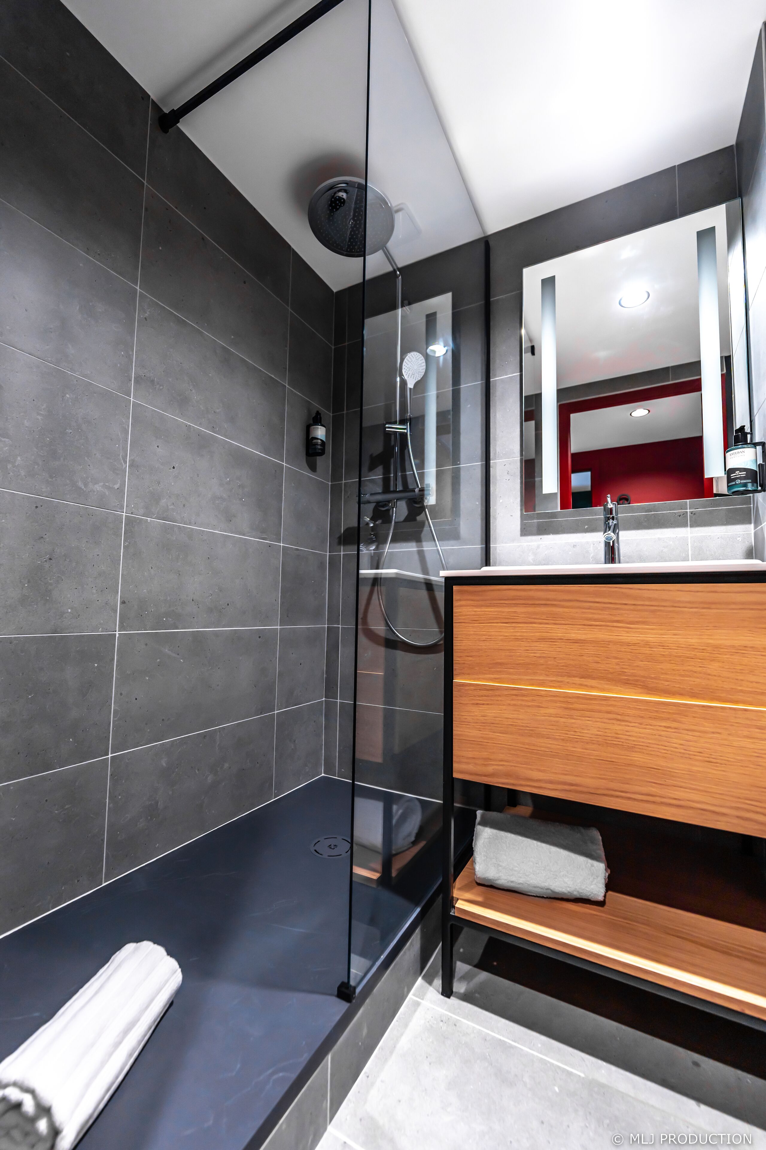 A modern bathroom with a glass shower enclosure, a wooden vanity, and a large mirror.