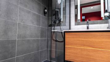 Un baño moderno con cabina de ducha de vidrio, tocador de madera y un espejo grande.