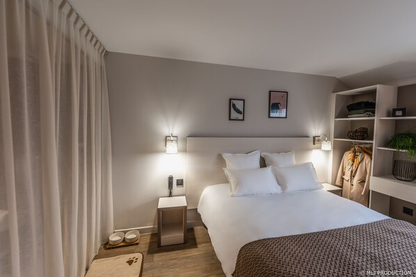 Une chambre d’hôtel moderne avec un grand lit, des tables de chevet, une armoire et un petit coin salon.
