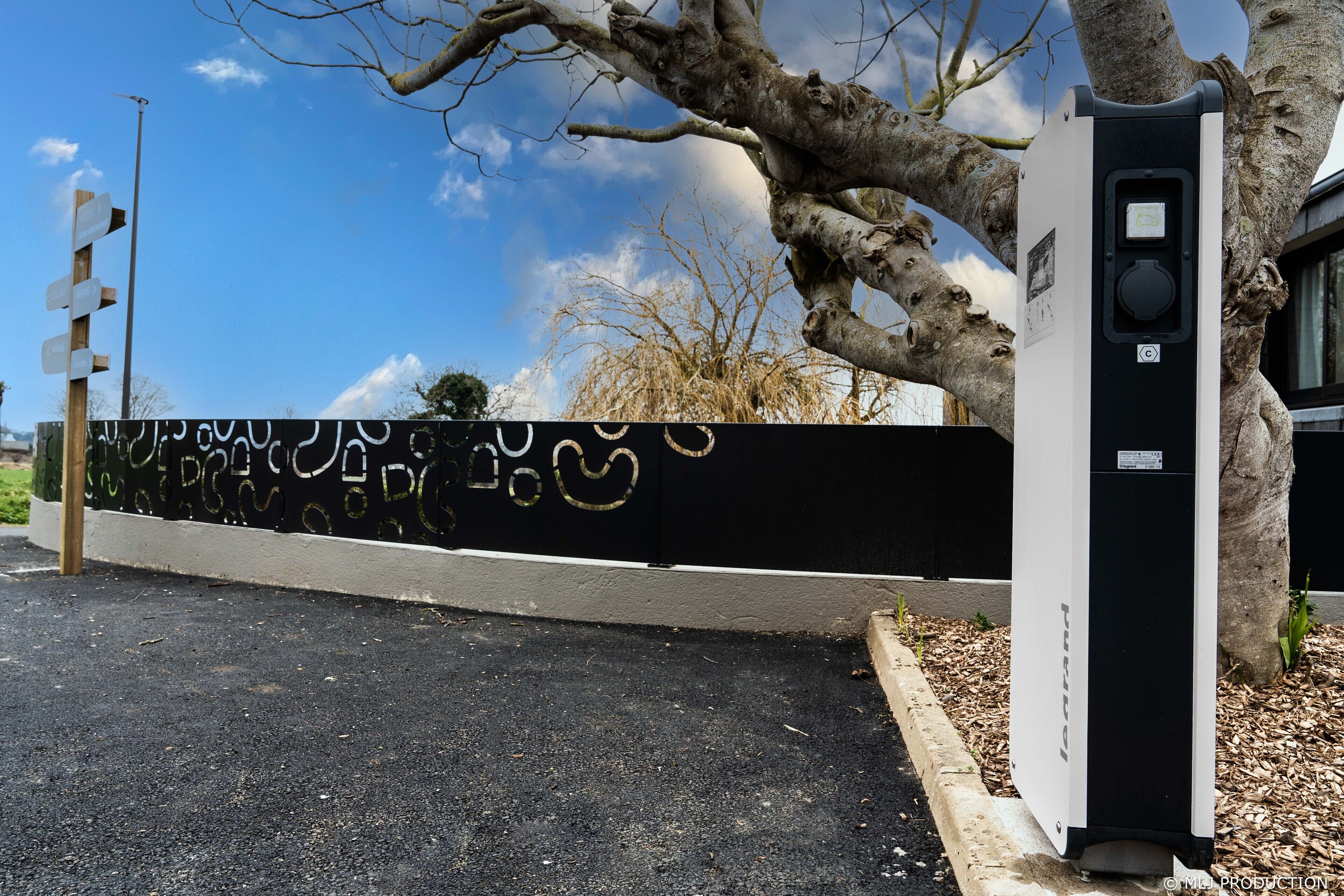 A parking area with a black and white wall, a tree, and a utility box.