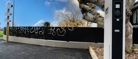 A parking area with a black and white wall, a tree, and a utility box.