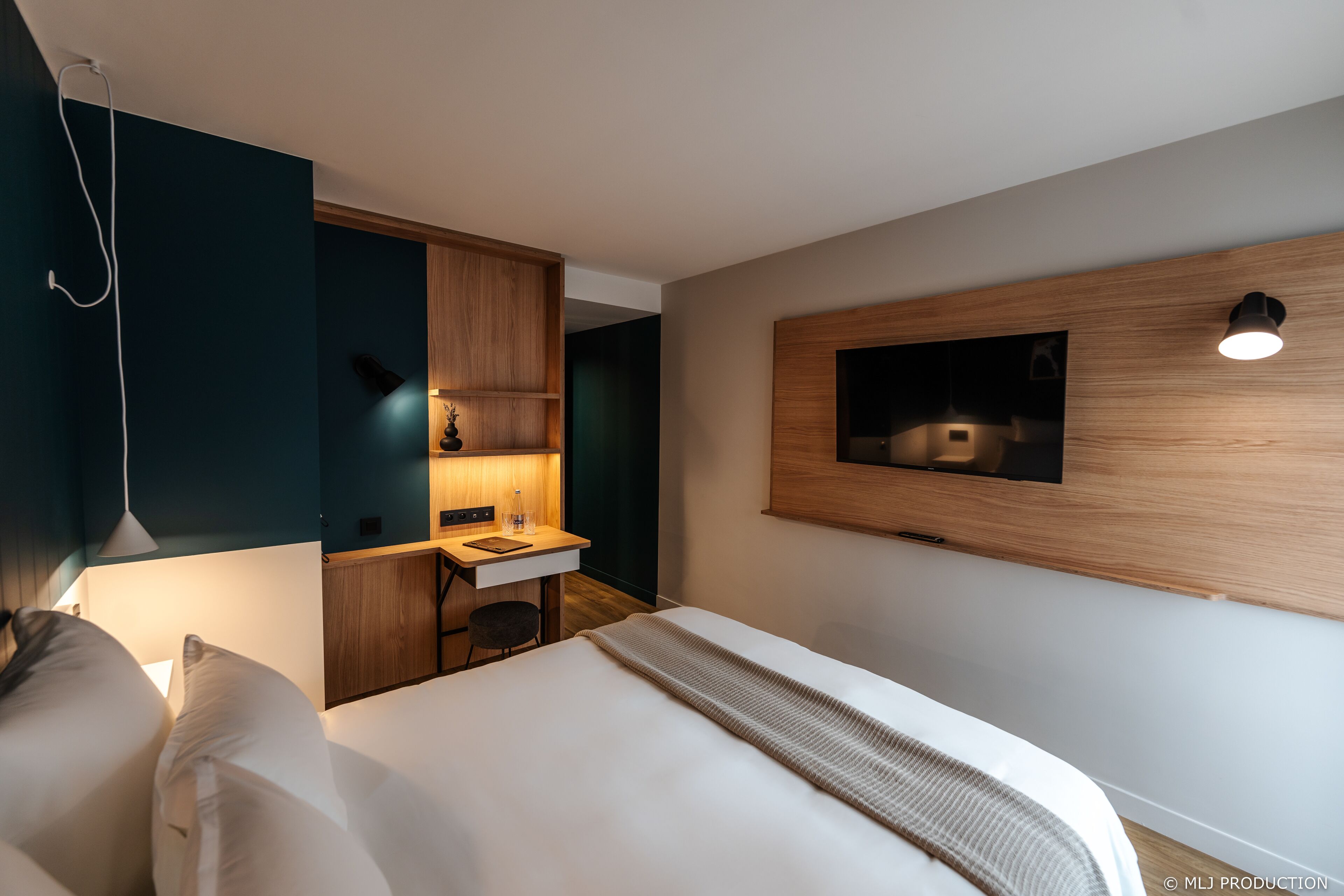 A modern hotel room with a bed, a desk, and a TV mounted on the wall.