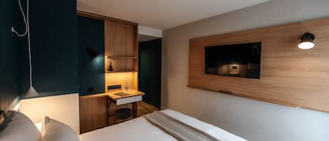 Ein modernes Hotelzimmer mit einem Bett, einem Schreibtisch und einem an der Wand befestigten Fernseher.