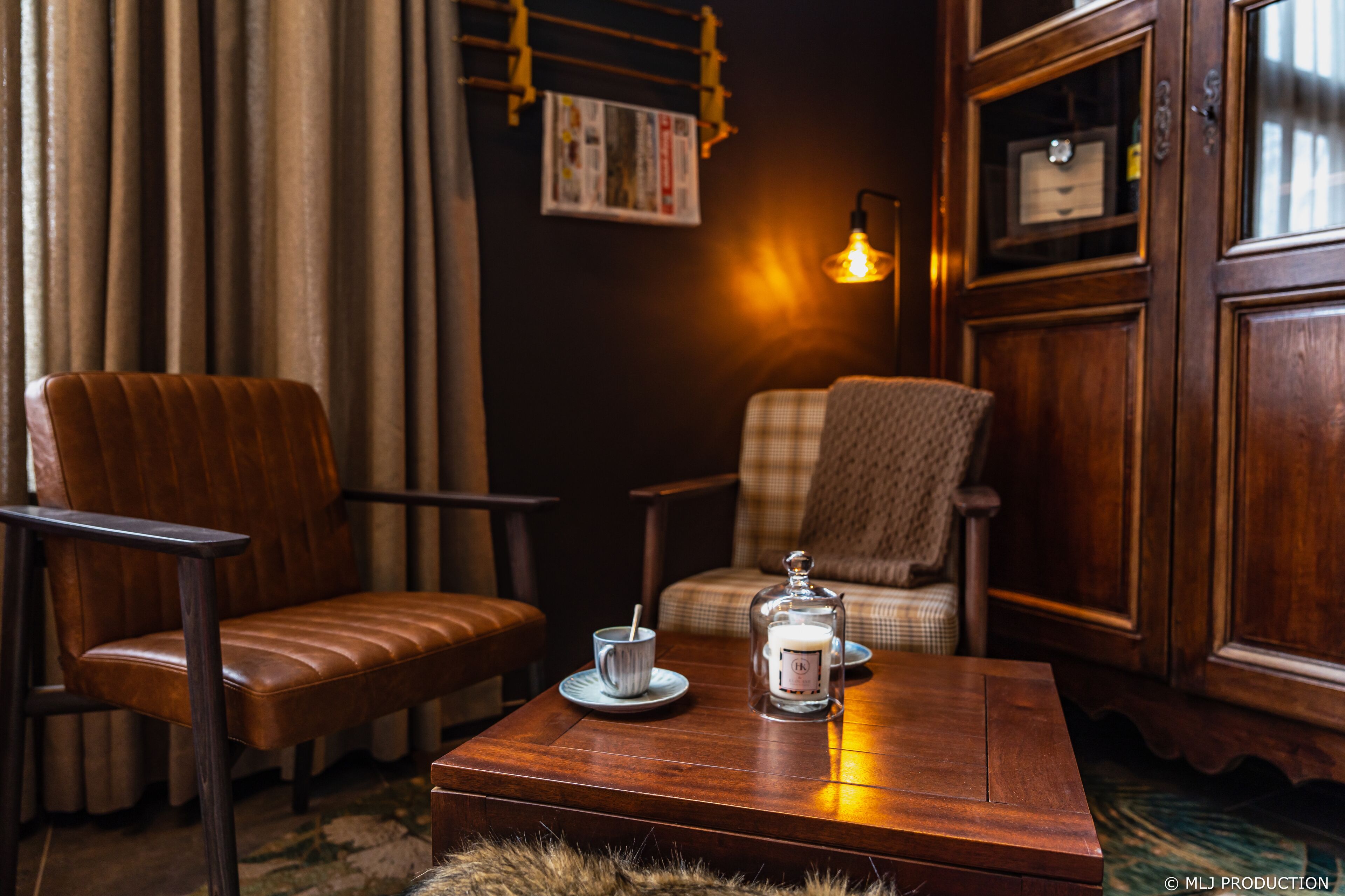 Una habitación acogedora con una mesa de centro de madera, dos sillones de cuero, un sillón estampado y una lámpara de pared, además de un candelabro de vidrio.